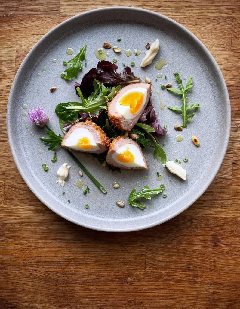 Crispy Scotch egg cut in half with a side of yellow mustard dip.
