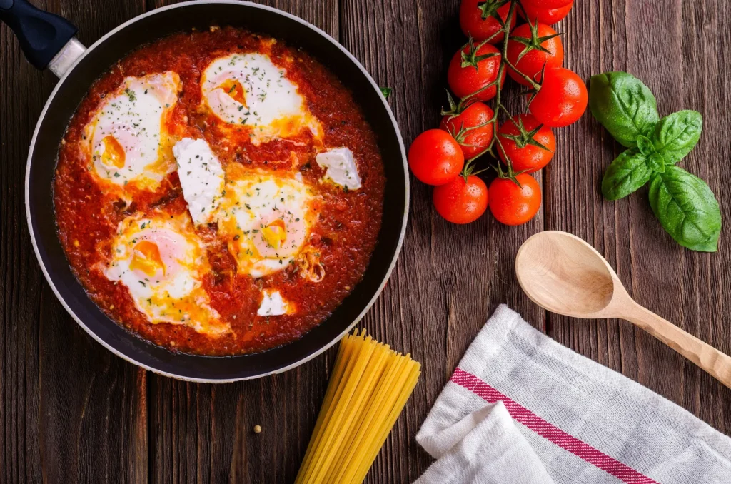 Close-up of a bubbling Shakshuka showing the contrast between the velvety orange egg yolks, the chunky tomato base, and the charred edges of sourdough bread dipped into the sauce.