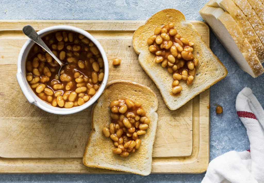 Beans on Toast served on a blue plate, featuring thick-cut sourdough topped with warm baked beans and a sprinkle of cheddar cheese.