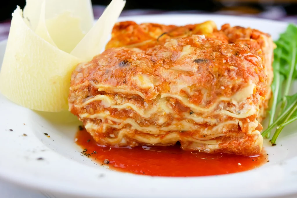 Beef lasagna slice being lifted from a baking dish, showing distinct layers of pasta, meat sauce, and gooey melted cheese.
