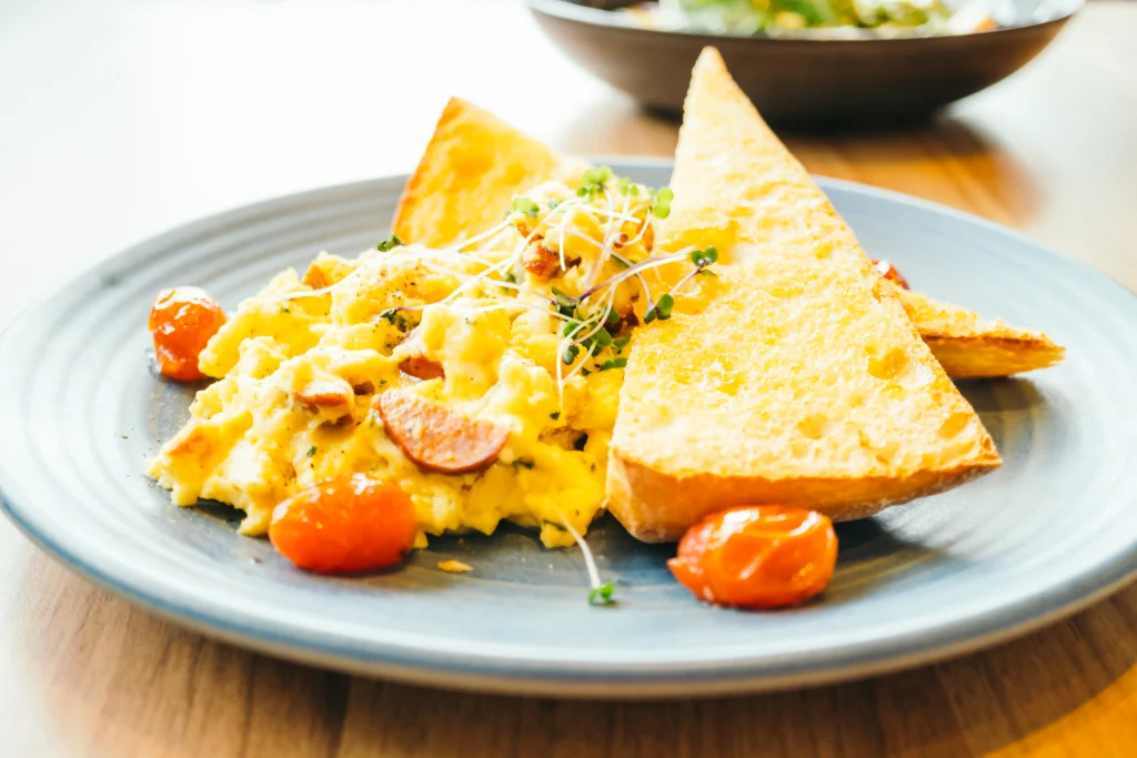 Close-up of fluffy creamy scrambled eggs piled high on a thick slice of toasted sourdough bread with fresh chives