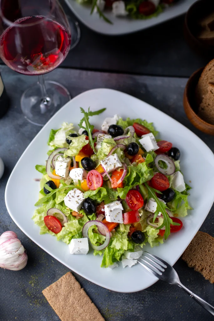 Greek Salad in a shallow bowl featuring large chunks of tomatoes, cucumbers, red onions, and a whole block of feta cheese topped with dried oregano.