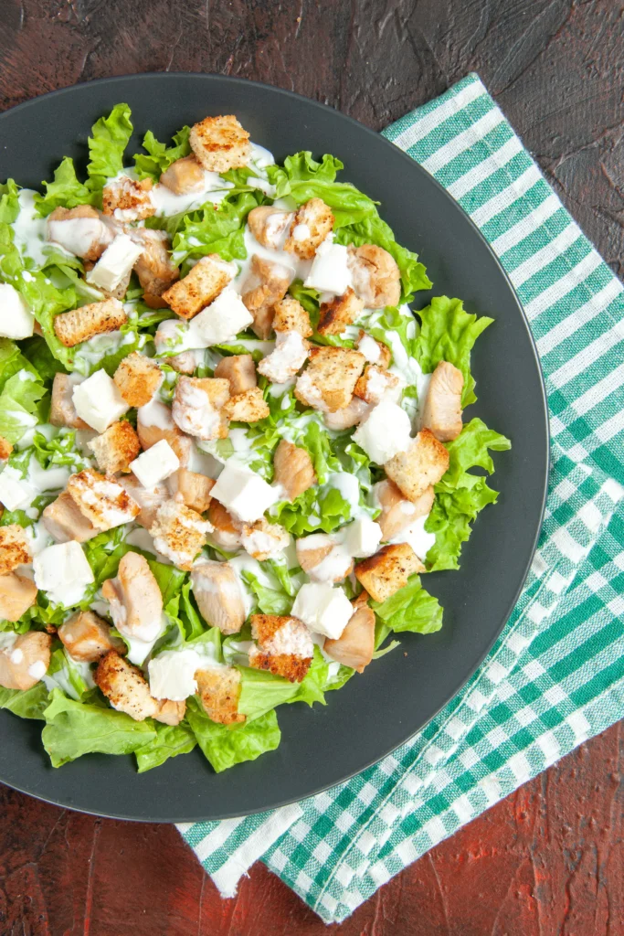 Classic Caesar Salad close-up, showing the crisp texture of fresh romaine lettuce leaves coated in a thick, garlic-infused black pepper dressing.