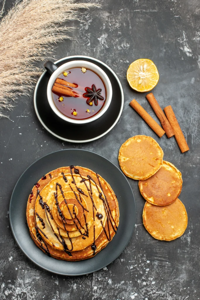 Folded lace pancakes on a plate garnished with fresh lemon slices and a dusting of sugar.