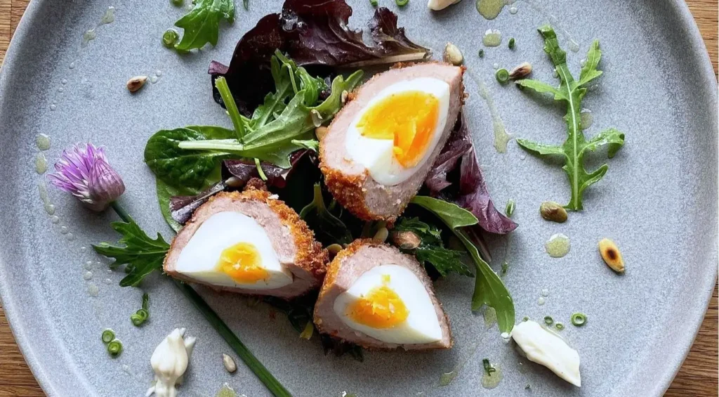 Handmade Scotch egg with a soft-yolk center and golden breading, served as a gourmet appetizer with spicy mustard dip